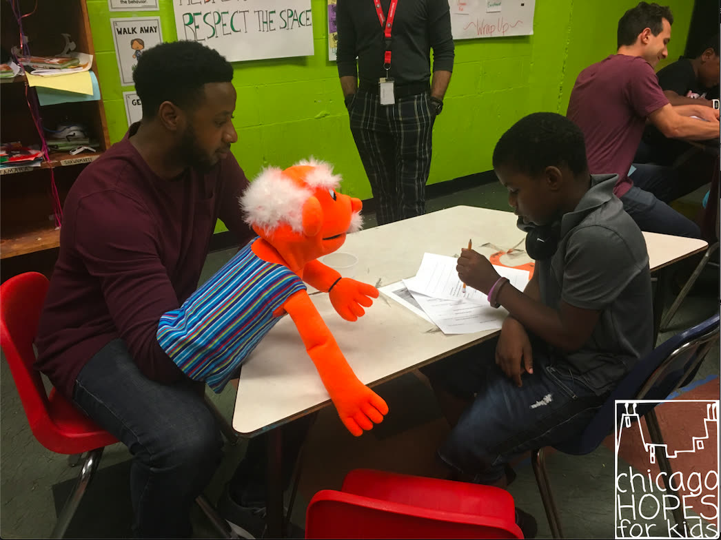 A teaching artist and a puppet helping a student with a worksheet